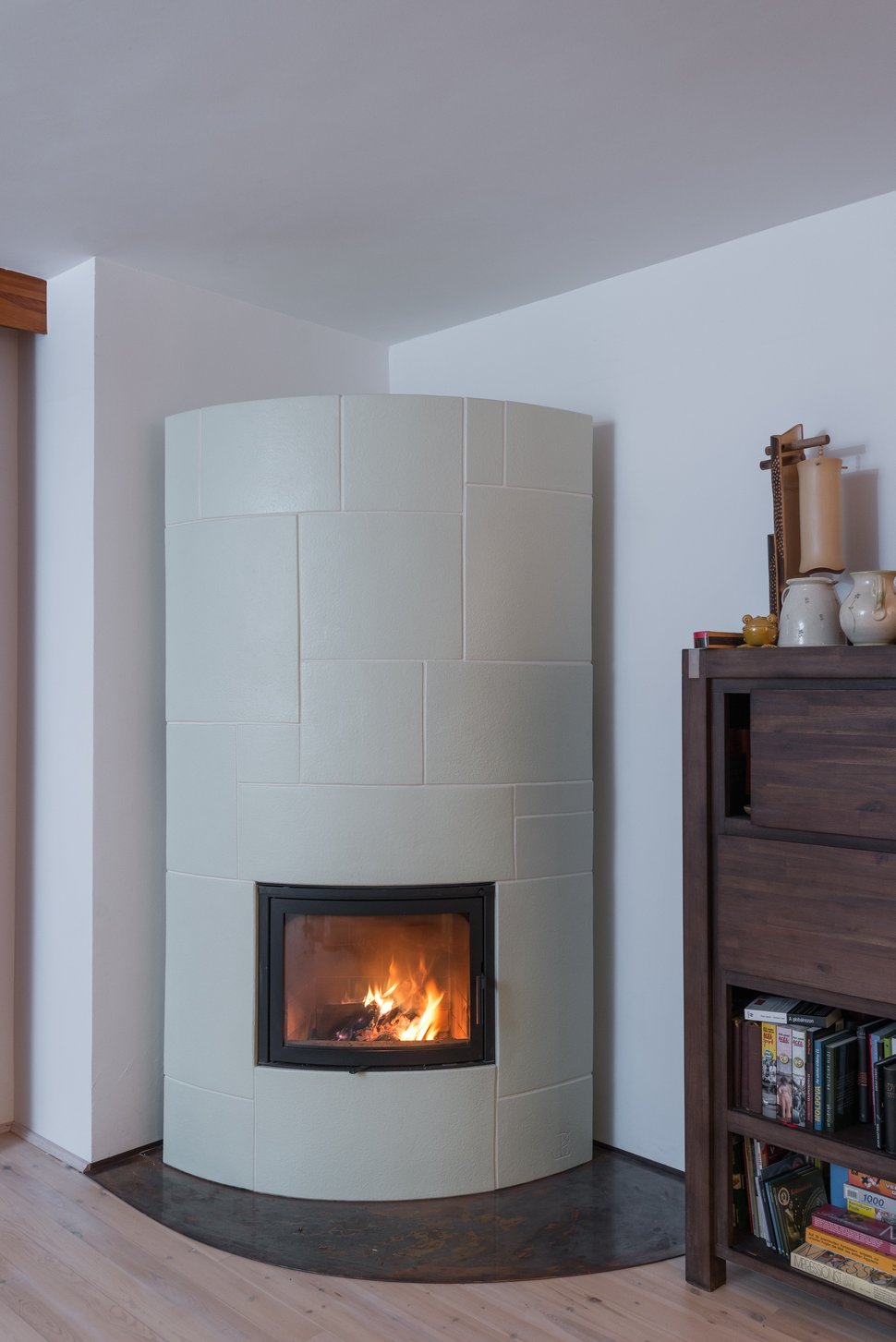 The white stove with a lit firebox in a pale, minimally furnished room.