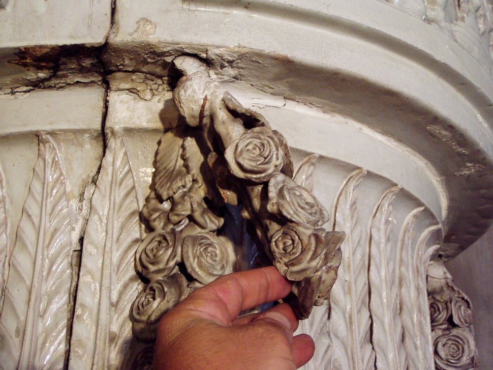 A hand touching a plaster rose ornament on the stove.
