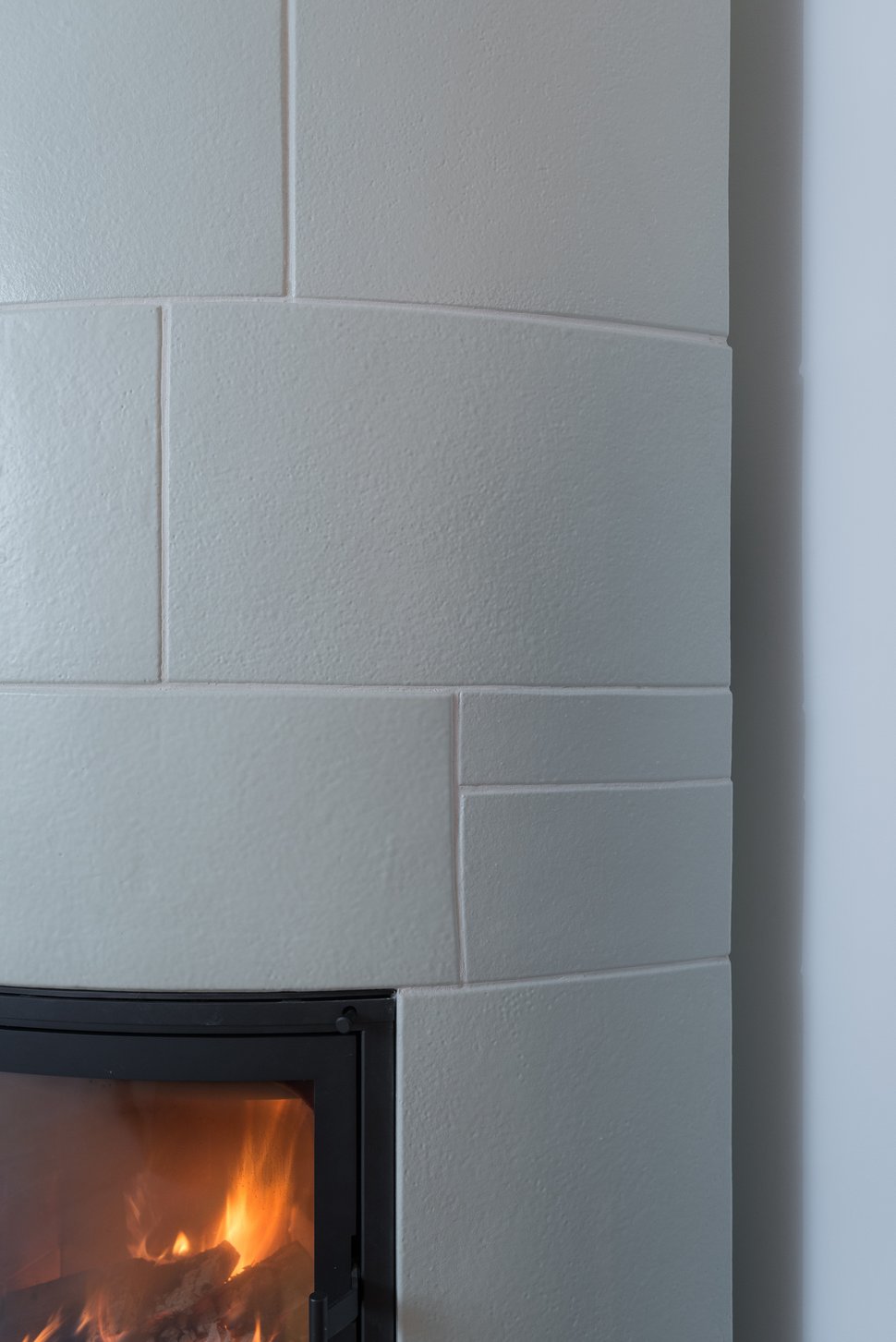 Close-up of the white stove's curved tiled corner above the firebox.