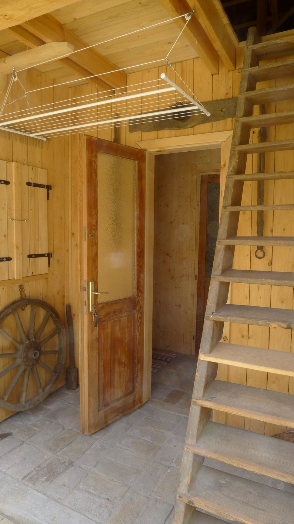 The sauna entrance with wooden stairs, a door and a cart wheel.