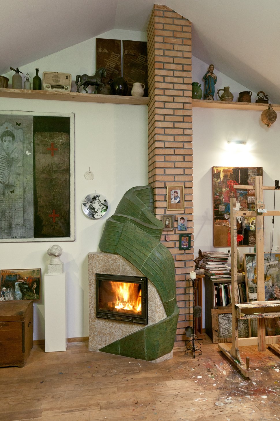 The green stove in the studio, surrounded by paintings and tools.