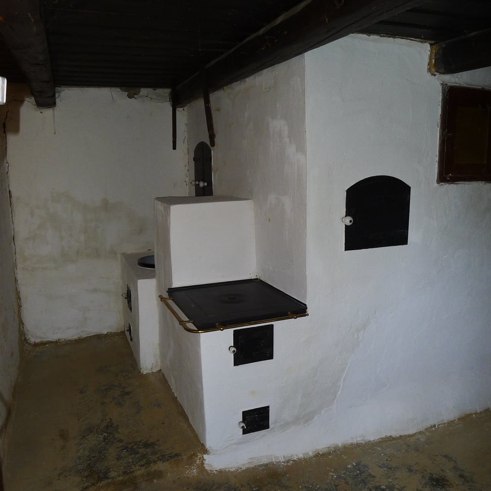 The completed white masonry stove with black doors in an attic room.