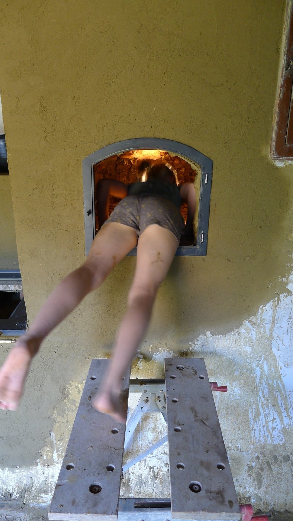 A child's legs emerging from a wall oven above a step stool.