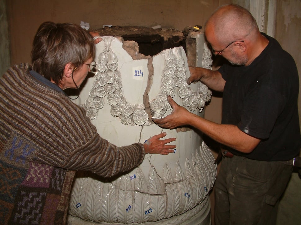 Two men examining numbered white stove pieces.