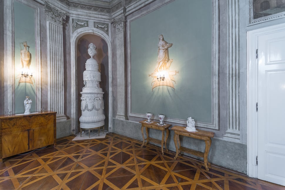 A tall white tiled stove in an ornate palace room with painted walls.