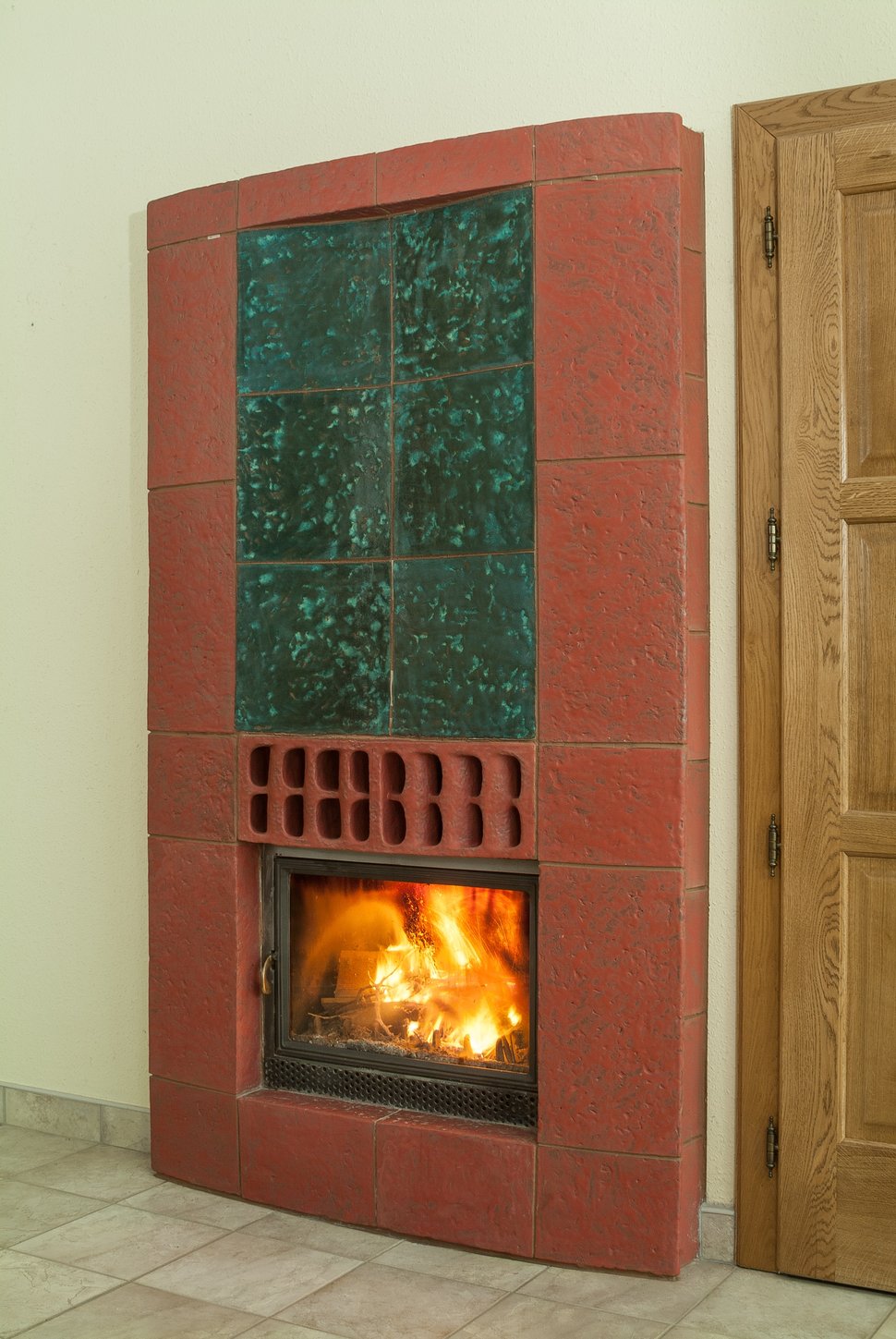 A red-framed stove with a green tiled panel beside a wooden door.