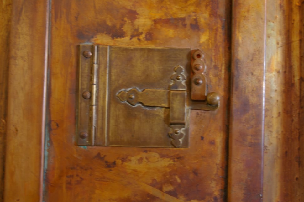 A cast-iron latch plate on a copper door, with a keyhole.