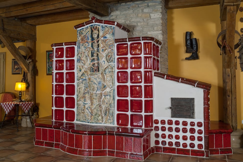 A red tiled stove with patterned tiles in a rustic wooden room.