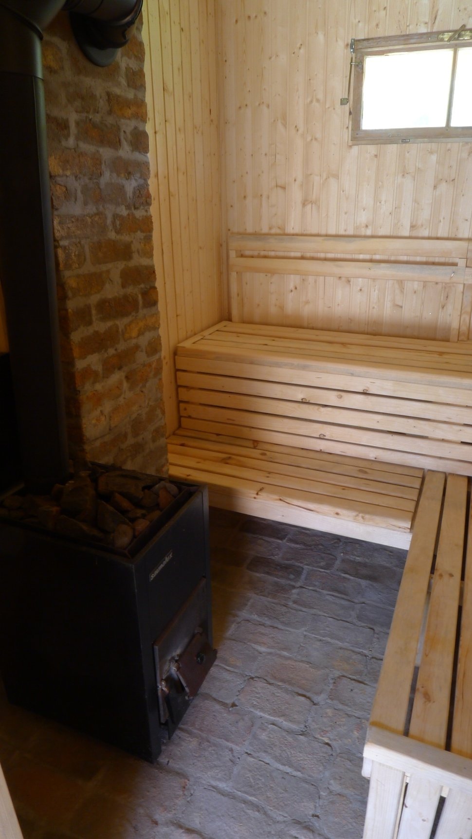 Inside the sauna, wooden benches and a black stove beneath a small window.