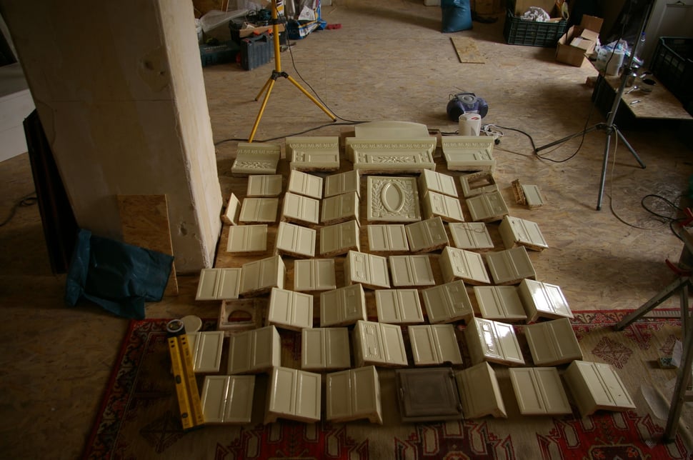 Rows of dismantled stove tiles laid out on a rug in a workshop.