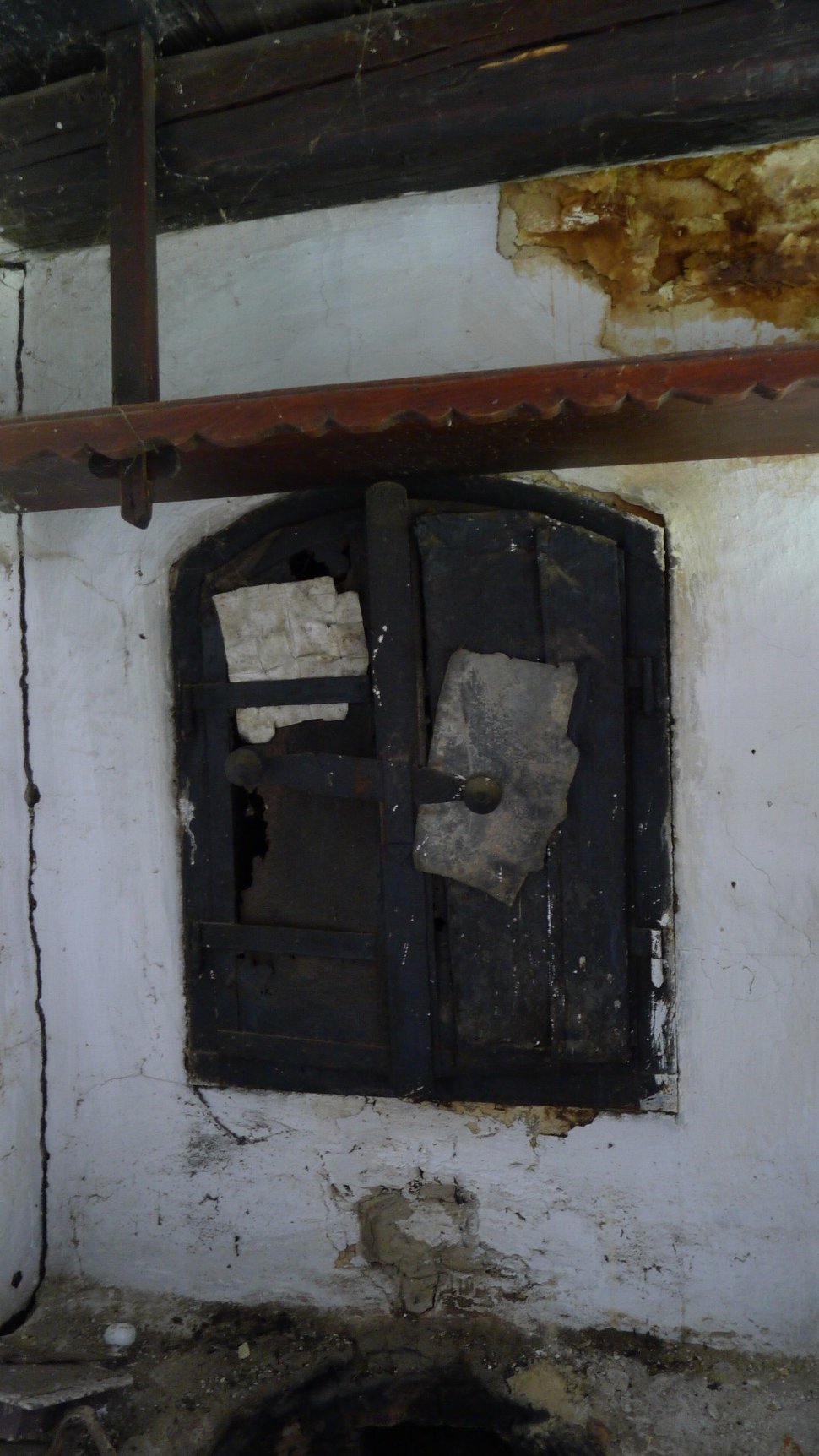 An old black smoke chamber door set into a white plaster wall.