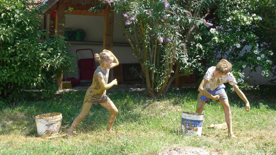Two children playing with buckets on the grass beside a house.