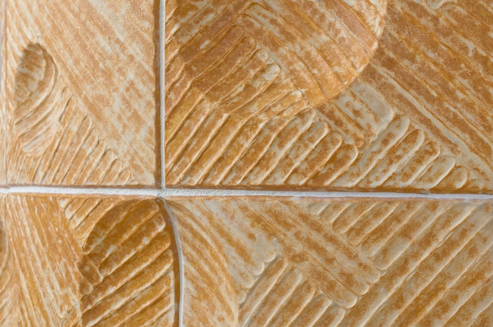 Carved cream tiles with fan and leaf patterns, joined by pale grout.