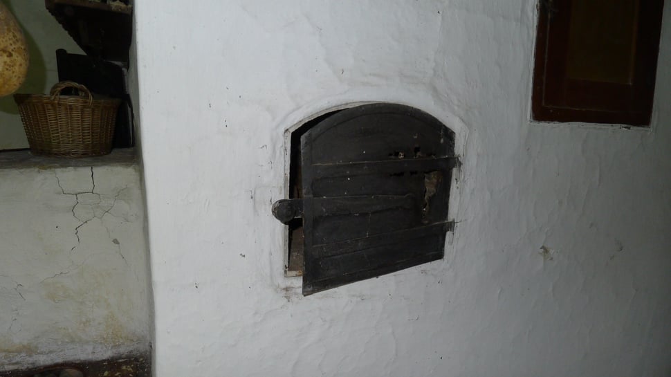 An old black oven door in a white plaster wall.