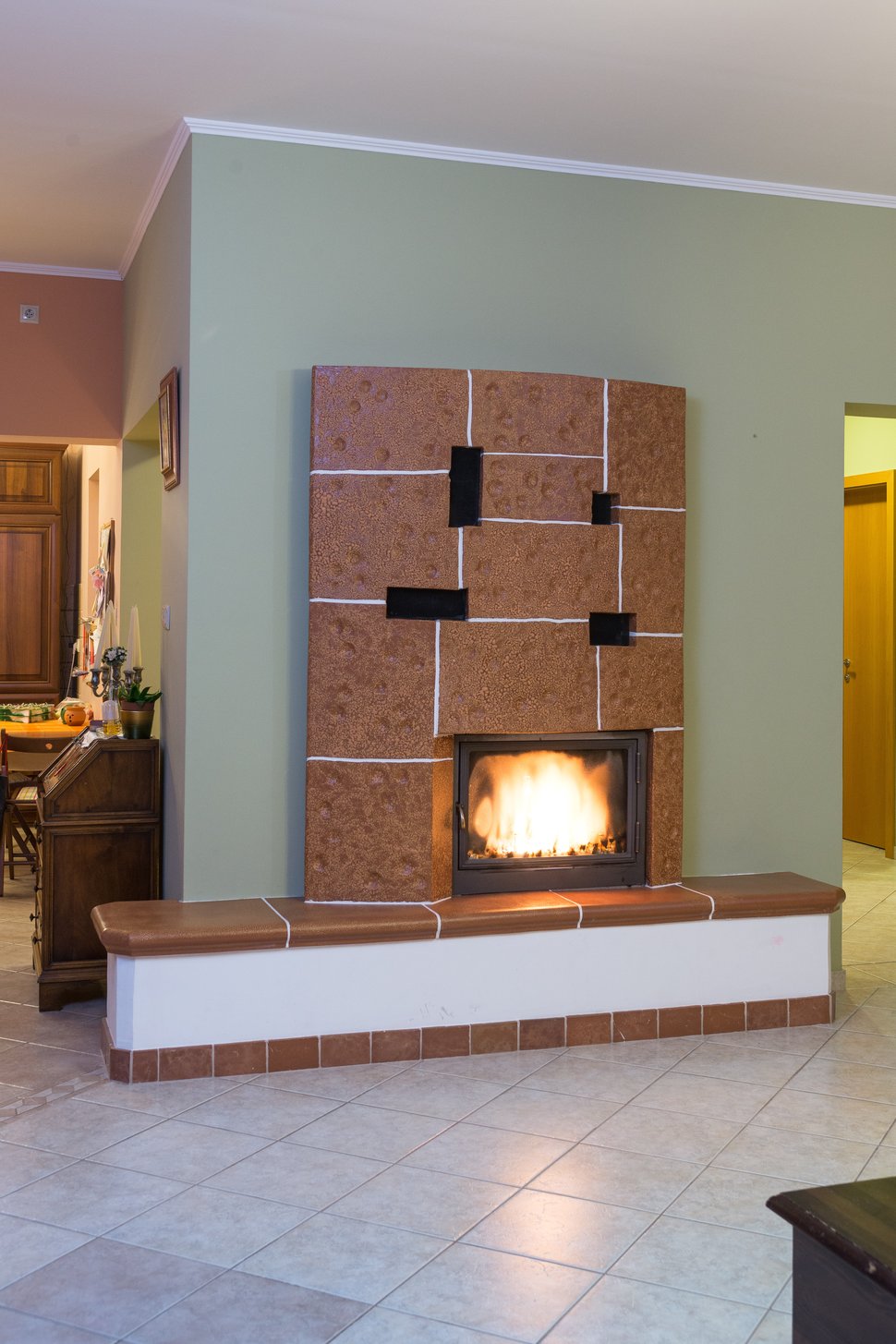 A brown tiled stove in a living room with a green wall.
