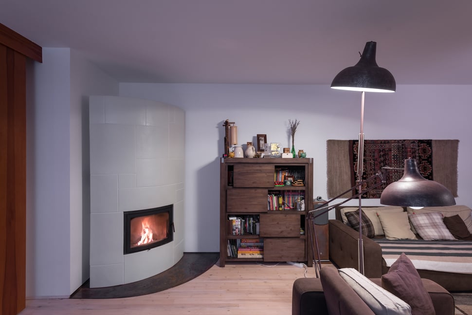 The white stove in a living room with a bookshelf and low lamp.