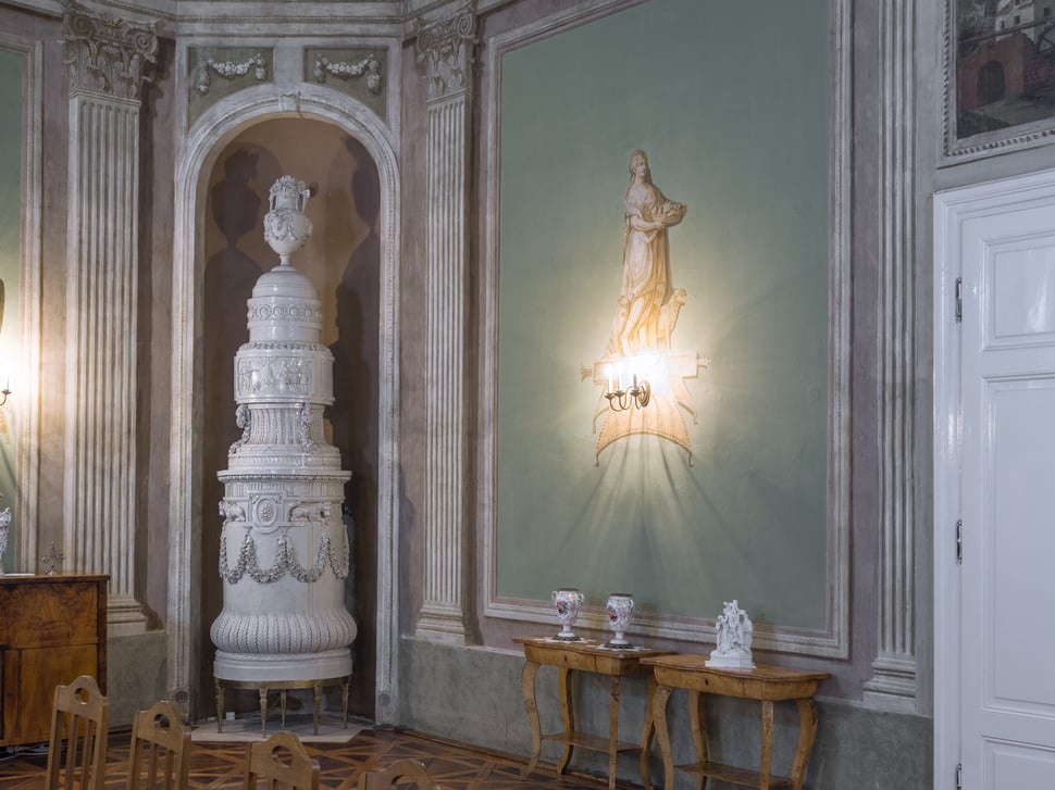 A tall white tiled stove in an ornate palace room.