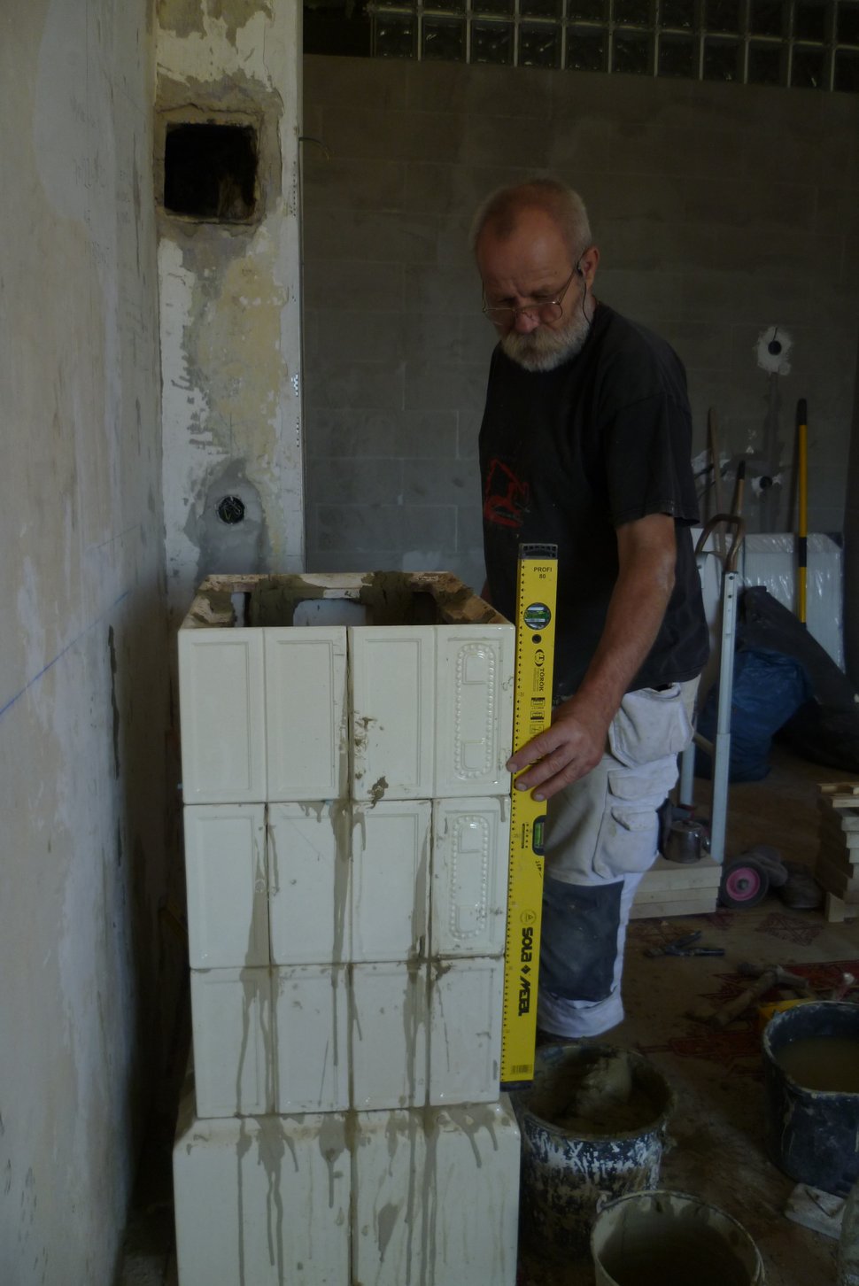 A man measuring a stack of stove tiles beside a wall.