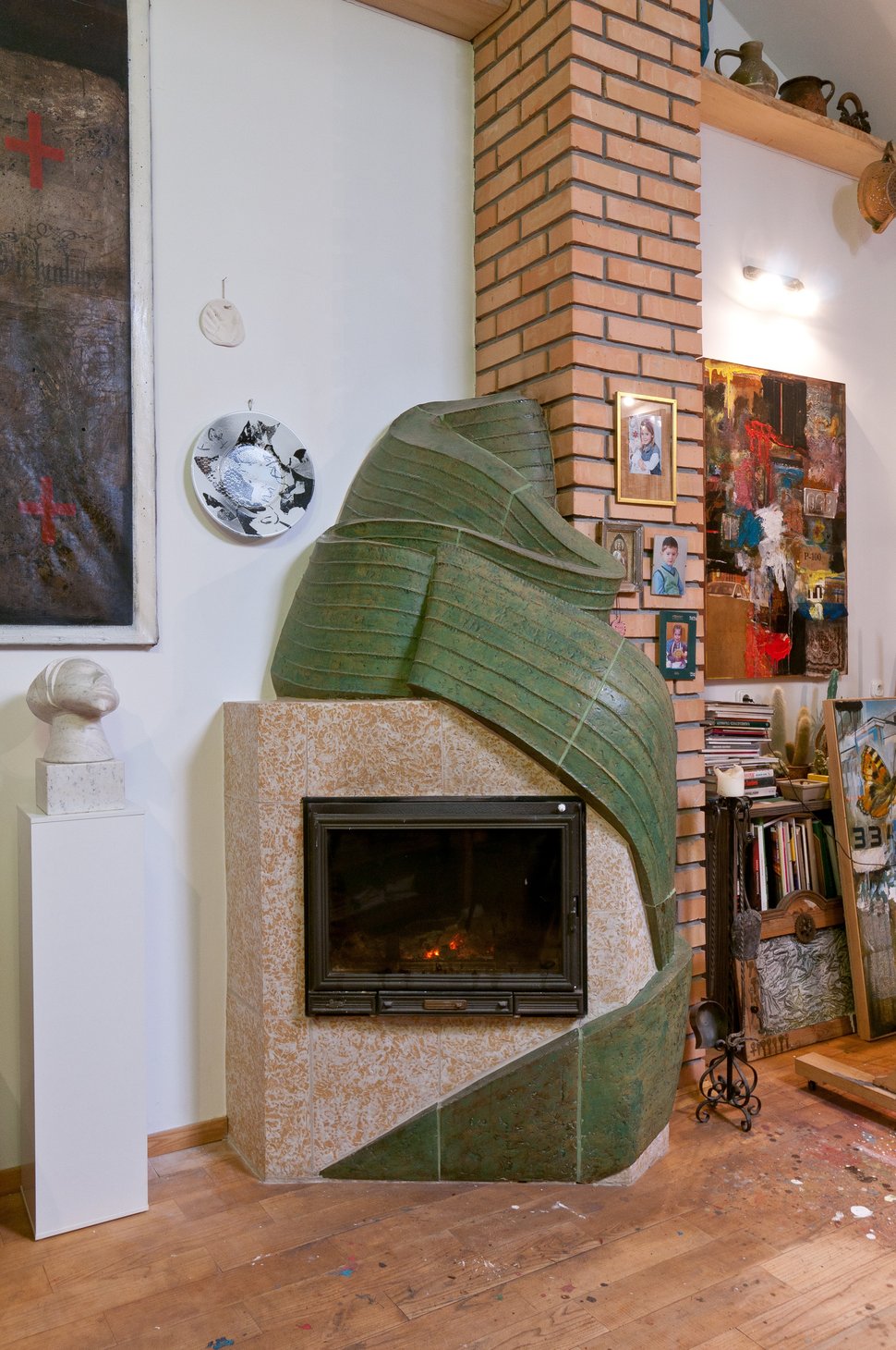 A green sculptural stove in an artist's studio, beside a brick chimney.