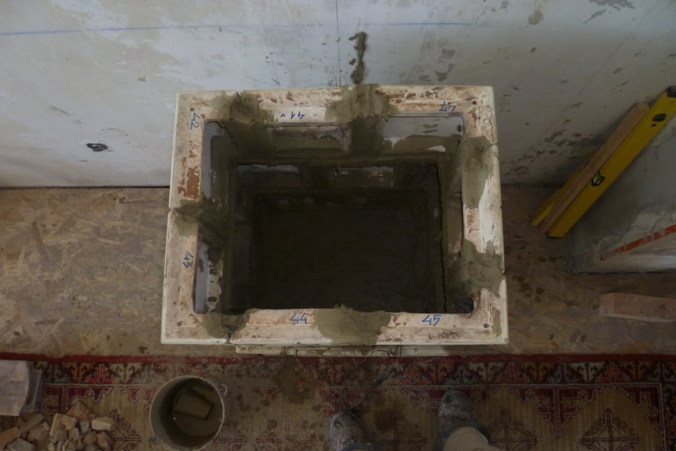 An empty square opening in a floor, with tools and a level nearby.