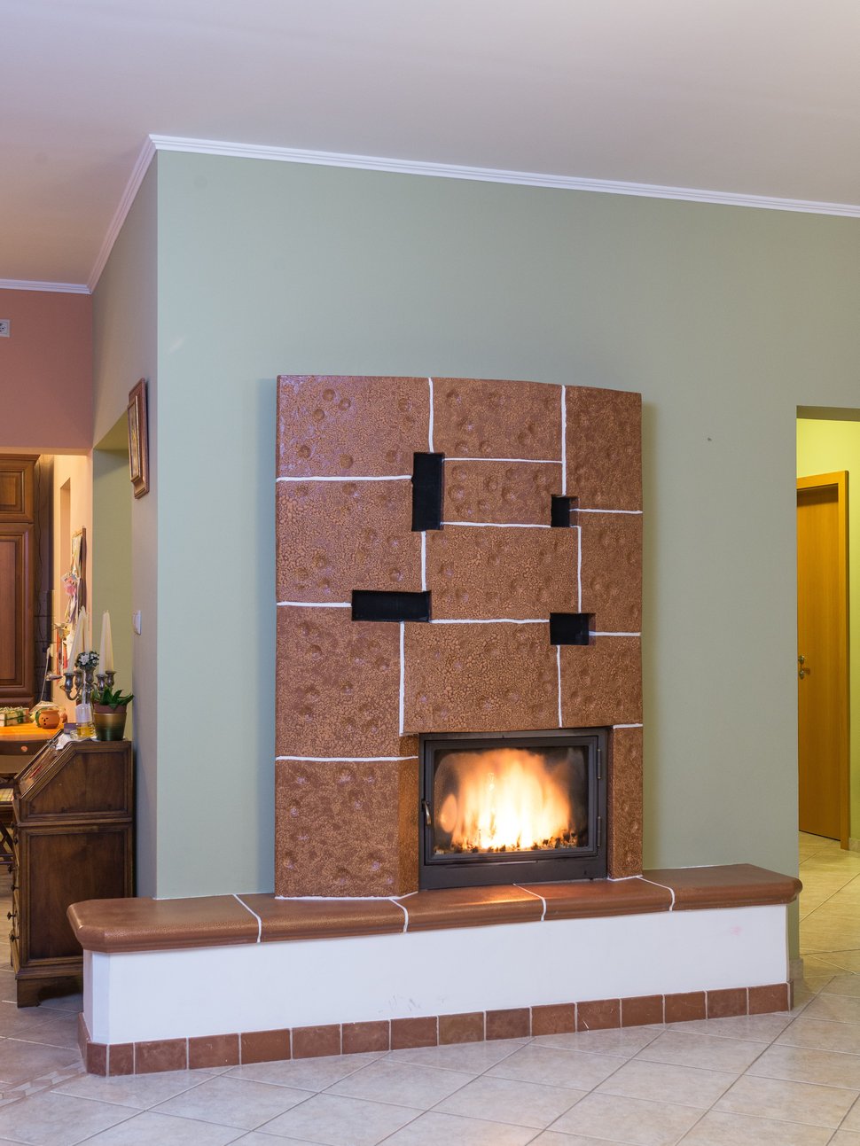 A tall brown speckled tiled stove with a firebox, set into a pale green wall.
