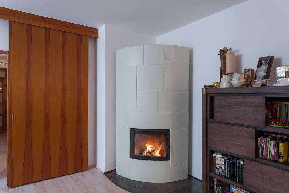 A cylindrical pale tiled stove in a living room with a wooden floor.