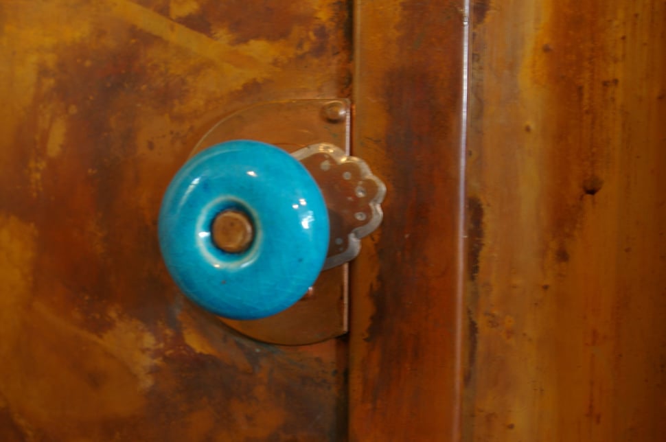 A turquoise ceramic knob on a copper door.