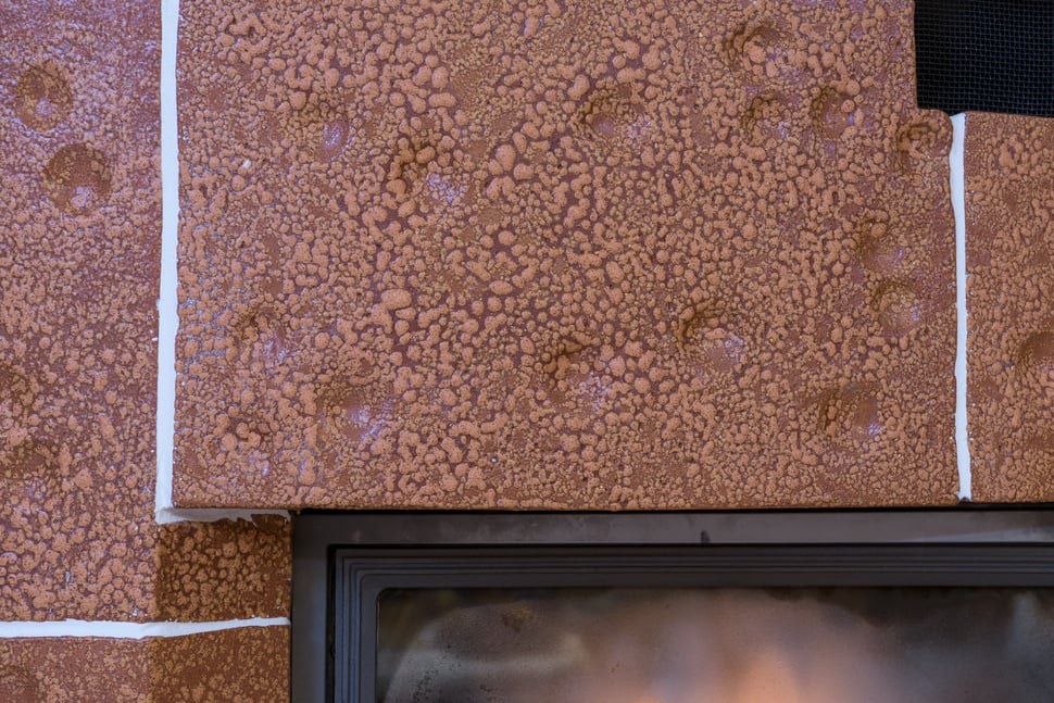 Close-up of brown glazed tiles and the black handle of the stove firebox.