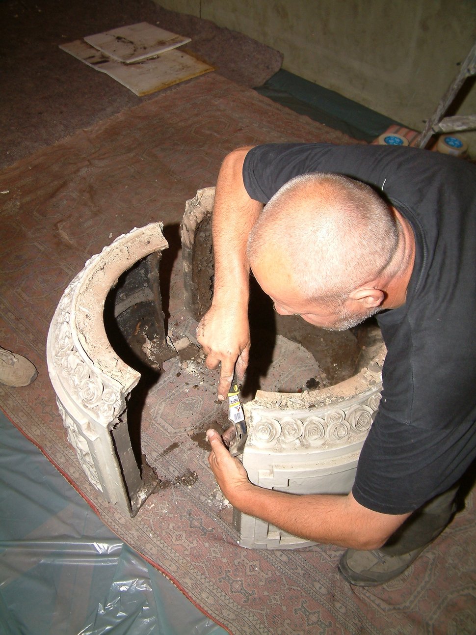 A man reaching inside the dismantled round base of a stove.