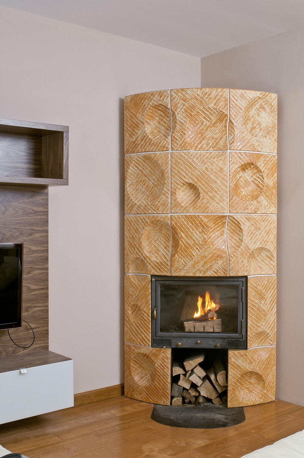 A cylindrical tiled stove with carved patterns beside a pale wall.