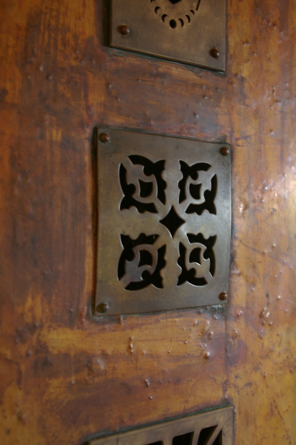 A cast-iron decorative grille on a mottled copper surface.