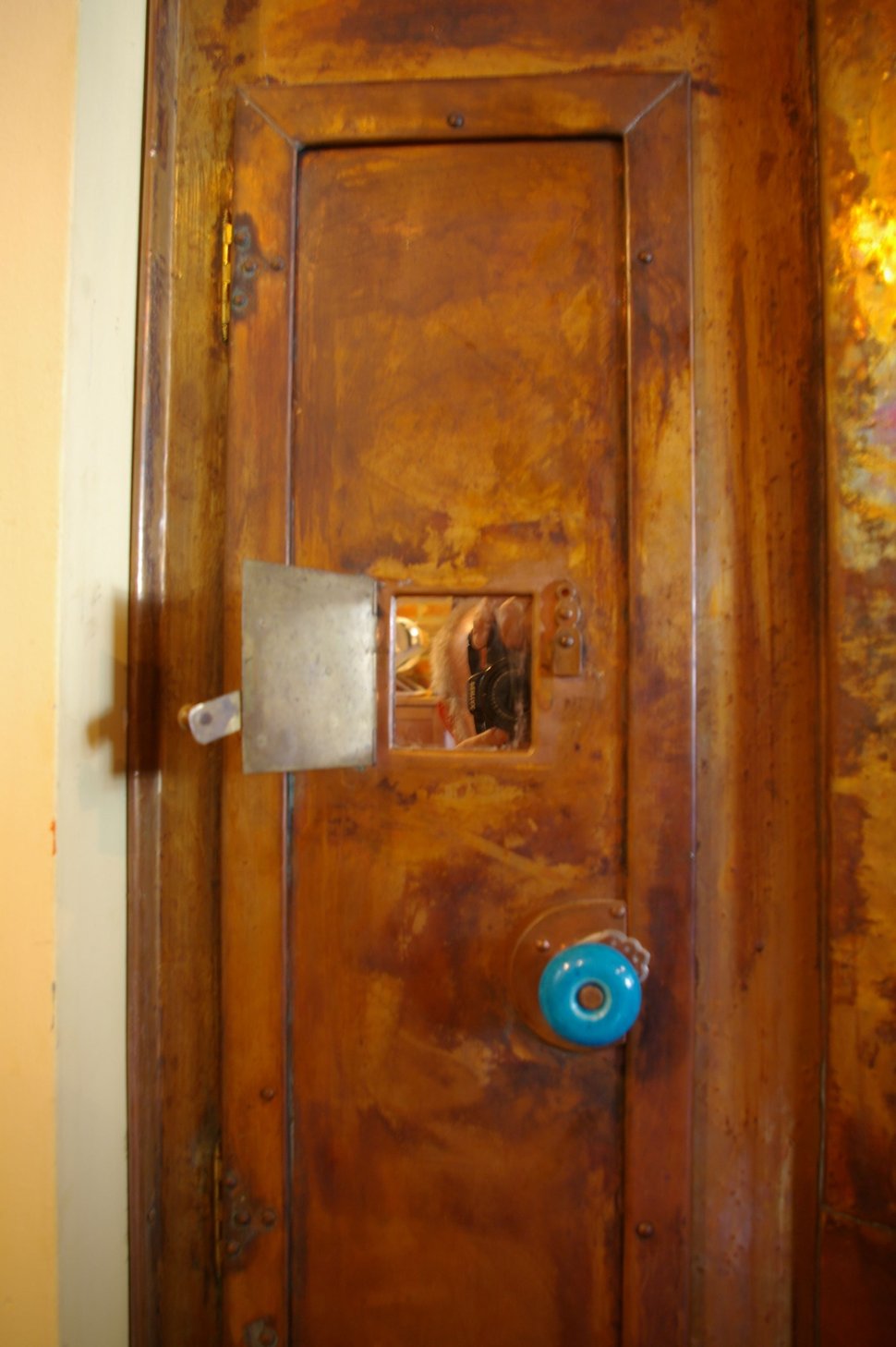 A copper door with a metal latch and a blue ceramic knob.