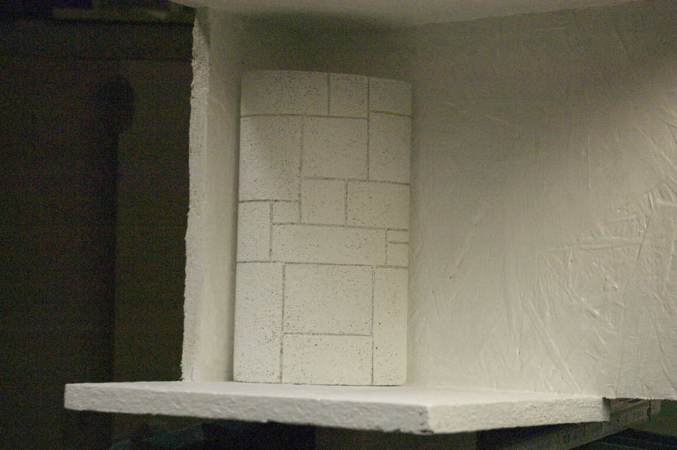 A pale tiled stove form with rough plaster, in a room under construction.