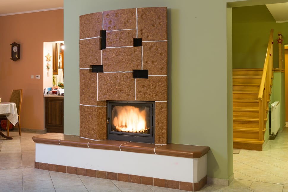 A brown speckled tiled stove with a white base, lit in a green room.