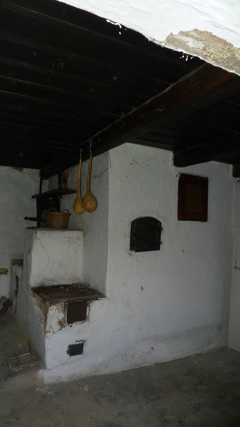 An old white masonry stove with a smoke chamber under a dark ceiling.