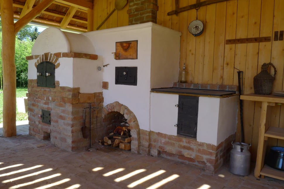 An outdoor masonry stove with a white dome and brick base beside the house.