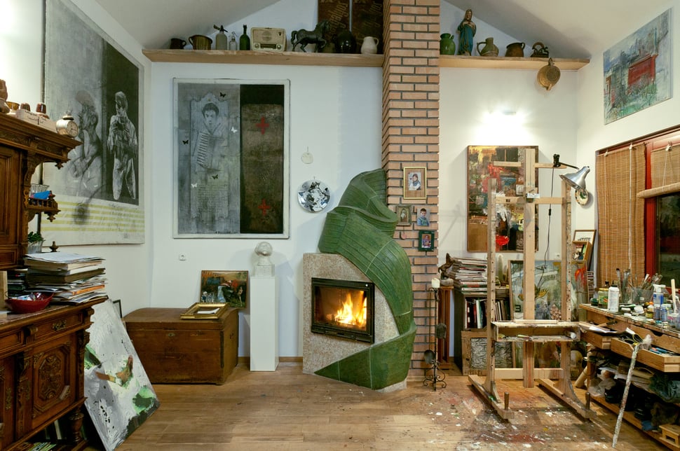 The studio with the green stove, easels, paintings and a wooden floor.