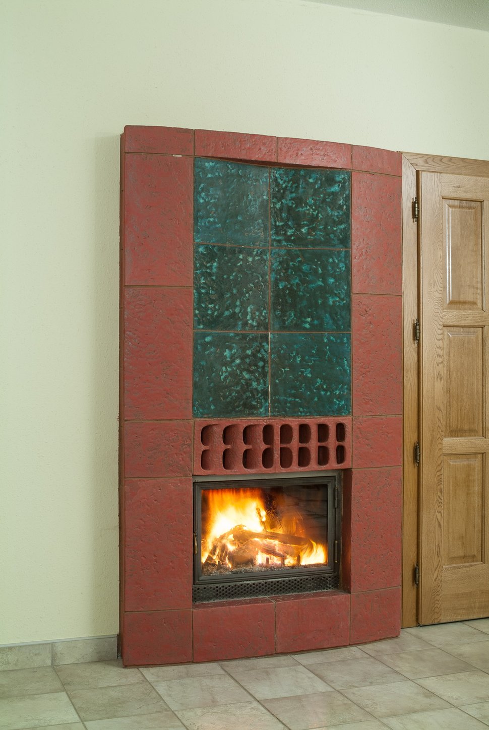 A red-framed stove with a green tiled panel and a lit firebox.